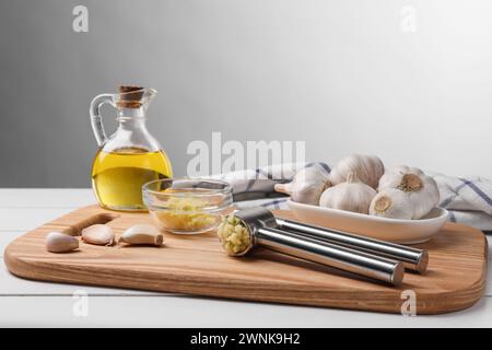 Una pressa in metallo e aglio schiacciato su un tavolo di legno bianco Foto Stock