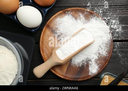 Composizione piatta con lievito in polvere e uova su un tavolo di legno nero Foto Stock