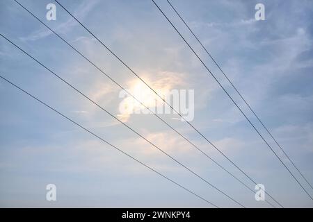 Linee di trasmissione ad alta tensione sospese diagonalmente contro il cielo blu con nuvole e sole splendente. Spazio vuoto. Griglia elettrica sopra la massa. Foto Stock