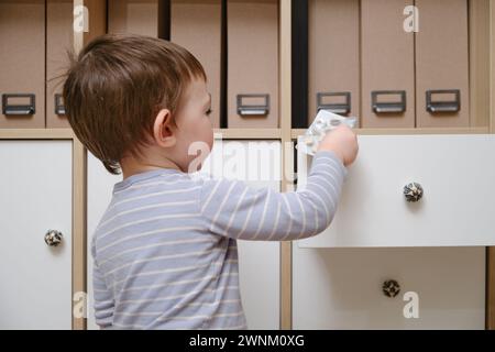 Il bambino del bambino ha aperto il cassetto dell'armadietto con le pillole e la medicina. Bambino che tiene una confezione di pillole nel salotto di casa. Bambino di età un anno nove mese Foto Stock