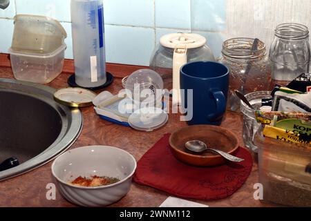 Numerosi piatti, piatti, bicchieri, cucchiai e vasetti si trovano a caso sul tavolo della cucina. Foto Stock