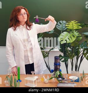 Donna ecologa con matraccio chimico e imbuto per liquido in mano. Analisi, test e ricerca nel laboratorio scolastico Foto Stock