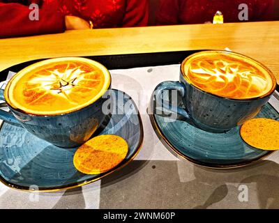 un paio di tazze di terra e un piatto contenente cappuchino serviti in un bar del tè Foto Stock