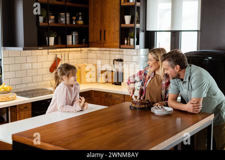 Una scena emozionante si svolge mentre una famiglia assaggia insieme una deliziosa torta al cioccolato nel calore della sua cucina soleggiata, condividendo sorrisi e sorrisi Foto Stock