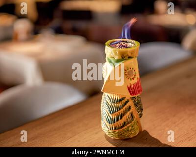 Tiki beve cocktail con zollette di zucchero bruciato. Cubo di zucchero bruciato in mezzo lime sul cocktail tiki al bancone del bar. Cocktail Tiki in totem Bird Mug con fuoco al bar nel night club o all'interno del ristorante Foto Stock