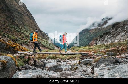 Coppia di escursionisti che attraversano il fiume con un ponte di legno sul percorso di trekking di Mera Peak vicino a Kothe. Uomo e donna che tornano a valle e si godono il Makalu Bar Foto Stock