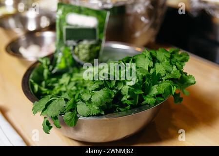 Una ciotola in acciaio inox riempita con foglie di coriandolo verde brillante, pronta per esaltare il sapore in vari piatti. Foto Stock