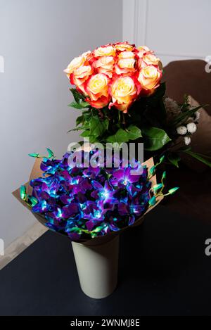 Uno splendido bouquet di rose fresche e luminose ed esotiche orchidee blu disposte in un vaso, perfetto per un regalo o una decorazione. Foto Stock