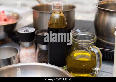 Una preparazione culinaria con olio d'oliva in una caraffa di vetro trasparente, aceto in bottiglia e macinacaffè per sale e pepe, pronti per l'insaporire. Foto Stock