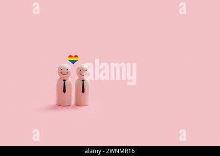 Felici figure gay di legno isolate su uno sfondo rosa. Ogni personaggio ha una semplice faccia sorridente e un piccolo cuore color arcobaleno sopra il Th Foto Stock