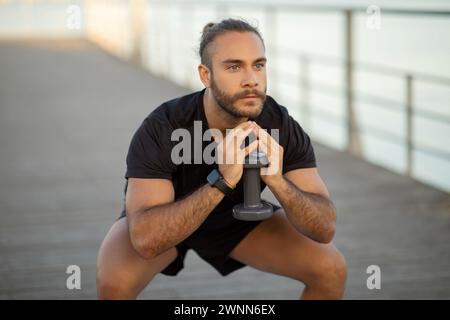 Atleta che esegue squat con pesi stupidi che si allenano all'aperto Foto Stock