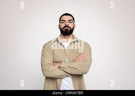Uomo sicuro di sé con una barba ordinata in piedi con le braccia incrociate Foto Stock