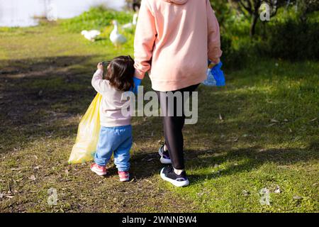 Donna e ragazza irriconoscibili che raccolgono rifiuti di plastica in un lago con oche sullo sfondo. Concetto di persone, riciclaggio, volontariato, natura Foto Stock