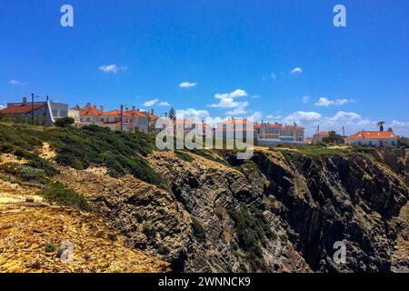 Città costiera con case dal tetto arancione su una scogliera, terreno roccioso in primo piano e un cielo azzurro. Foto Stock