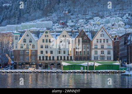 Paesaggio urbano sul lungomare di Bergen. Con le case di bryggen in stile chiaro di fronte al molo. Vista dall'altra parte della baia nelle fredde giornate invernali di neve. Foto Stock