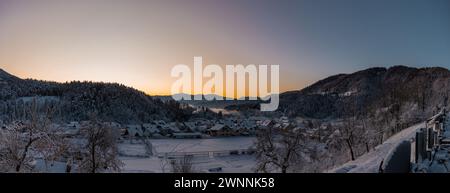 Panorama di case ricoperte di neve nel bellissimo villaggio di Ljubno ob Savinji, sede del salto con gli sci femminile. La mattina presto con il sole che sta per arrivare Foto Stock