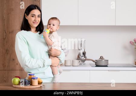 Madre che dà alla sua piccola rosticceria con il cibo in cucina Foto Stock