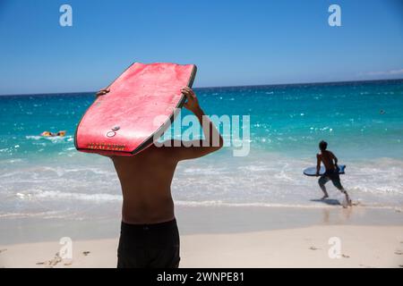 La gente del posto cavalca le onde su una spiaggia di sabbia bianca alle Hawaii. Foto Stock