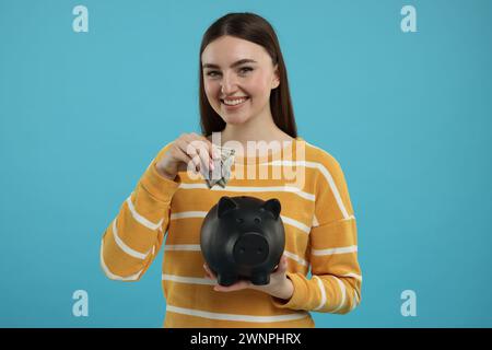 Donna felice che mette banconote da un dollaro nel salvadanaio su sfondo azzurro Foto Stock