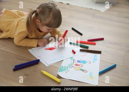 Bella bambina che disegna con un pennarello sul pavimento in interni. Arte dei bambini Foto Stock