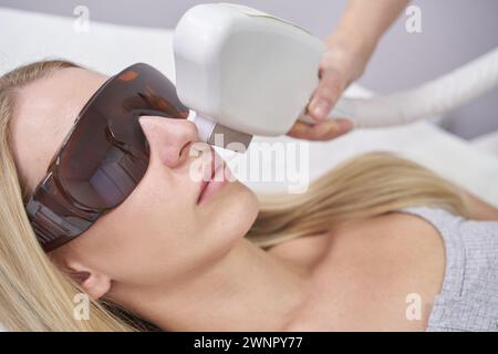 Trattamento viso laser per la depilazione e il ringiovanimento presso la spa. Le attrezzature bianche migliorano la bellezza e la cura della pelle. Il cosmetologo utilizza la tecnologia avanzata per la terapia, promuovendo la salute, la cura cosmetica Foto Stock