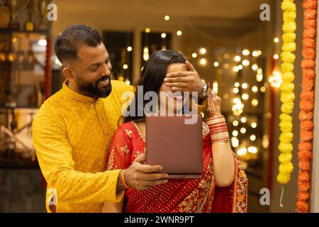 Il giovane marito indiano sorprende la moglie regalando preziosi gioielli in occasione dell'anniversario di Diwali o del matrimonio. Marito e moglie vestiti in stile tradizionale Foto Stock