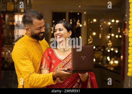Giovane marito indiano che regala alla moglie preziosi gioielli in occasione del Diwali o dell'anniversario di matrimonio. Marito e moglie vestite in abiti tradizionali su festiva Foto Stock