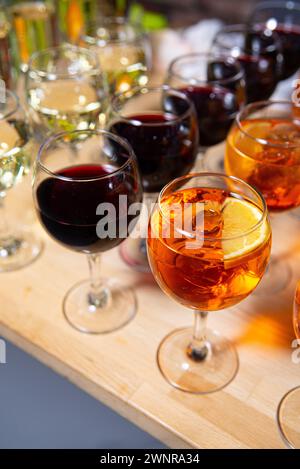 Varietà di bicchieri da vino pieni di vino rosso, bianco e da aperitivo, esposti su un tavolo di legno. Foto Stock