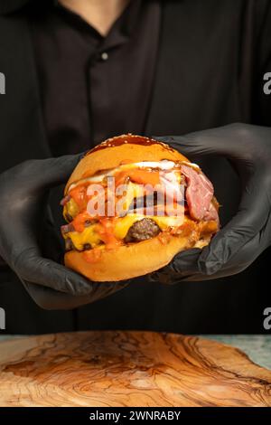 Doppio hamburger. Con formaggio Cheddar, cipolle caramellate, roast beef e salsa speciale. Sta tenendo un hamburger con due polpette in mano Foto Stock