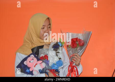 4 settembre 2023, una donna musulmana asiatica sta portando un secchio di fiori in mano. Wonosobo, Indonesia Foto Stock