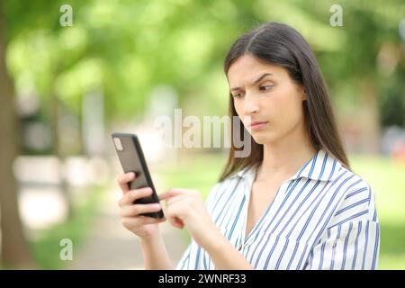 Donna sospetta che controlla strane notizie al telefono in un parco Foto Stock