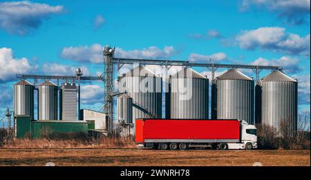 Semi-autocarro con rimorchio rosso davanti ai silos degli impianti di lavorazione dei cereali agricoli, attenzione selettiva Foto Stock