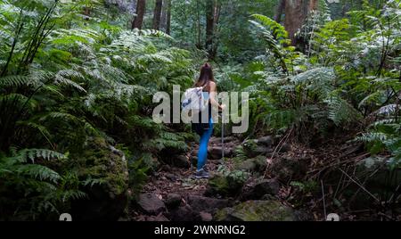Escursionista e backpacker vestita di blu con pali cammina lungo un sentiero tra la giungla di la Palma sull'isola delle Canarie Foto Stock