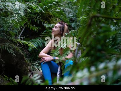 Una donna con zaino in spalla ed escursionista vestita di blu seduta nella giungla osservando la natura a la Palma, Isole Canarie Foto Stock