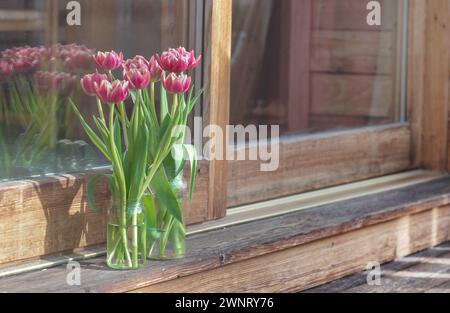 bouquet di tulipani in vaso di fronte a una finestra a bovindo su una terrazza in legno Foto Stock