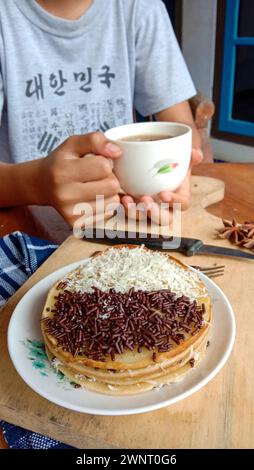 Una foto di qualcuno che mangia un mini martabak e beve una tazza di tè su un tavolo di legno Foto Stock