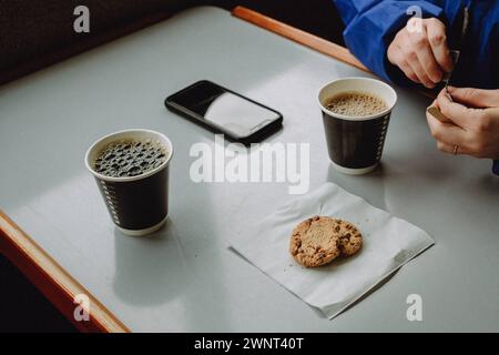 Pausa caffè al tavolo con tazze di carta e biscotti su tovagliolo Foto Stock