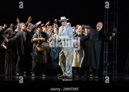 Lo scrittore e turista tedesco Gustav von Aschenbach (centro - cantato da Mark le Brocq) con venditori di strada veneziani nell'opera DEATH IN VENICE di Benjamin Britten al Welsh National Opera, inaugurazione al Wales Millennium Centre di Cardiff il 7 marzo 2024. Cinquantuno anni dopo la prima dell'opera ad Aldeburgh questa nuova produzione è diretta da Olivia Fuchs e successivamente tour a Llandudno, Southampton, Oxford, Bristol e Birmingham. Foto Stock