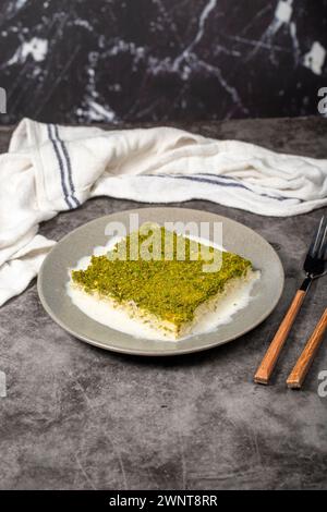 Kadayif freddo con pistacchio. kadayıf dessert al latte con pistacchi su sfondo scuro. Nome locale soğuk kadayıf tatlısı Foto Stock