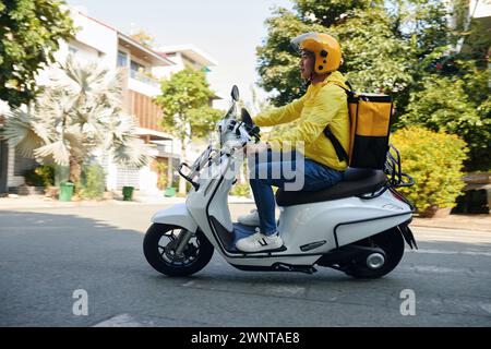 Vista laterale del giovane che lavora come corriere in moto Foto Stock