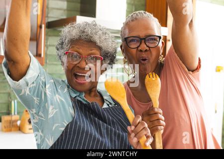 La donna afroamericana anziana e la donna birazziale anziana festeggiano con gli utensili da cucina Foto Stock