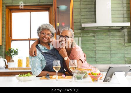 Una donna afroamericana anziana e una donna birazziale senior condividono un caldo abbraccio in una cucina Foto Stock