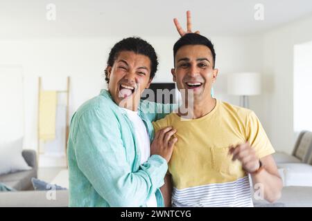 Il giovane uomo birazziale dà scherzosamente un segno di pace dietro la testa di un uomo sorridente del Medio Oriente Foto Stock