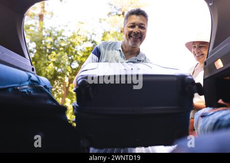 La coppia birazziale senior carica i bagagli in un'auto, pronta per un viaggio Foto Stock