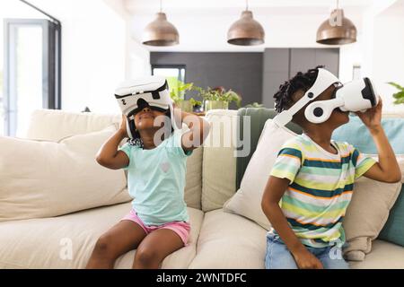 Sorella e fratello afroamericani sono immersi nella realtà virtuale, seduti su un divano Foto Stock