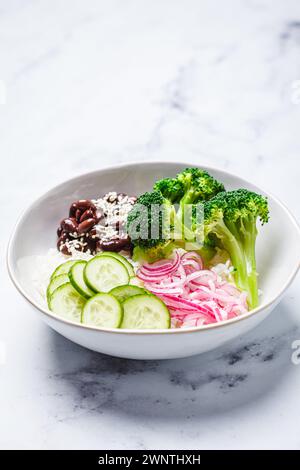 Ciotola vegana con riso, broccoli, cetriolo, fagioli e cipolla rossa sottaceto, sfondo in marmo bianco. Foto Stock