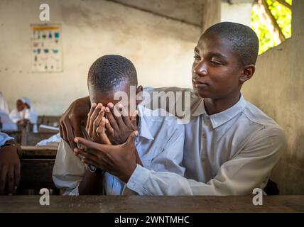 Uno studente musulmano conforta il suo amico in una classe di inglese alla Jambiani Secondary School di Jambiani, Zanzibar, Tanzania. Foto Stock