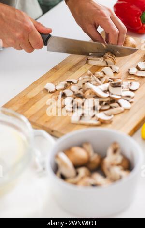 Le mani affettano i funghi su un tagliere di legno con un coltello da cucina Foto Stock