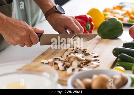 Una persona taglia i funghi su un tagliere bianco, circondato da peperoni colorati Foto Stock