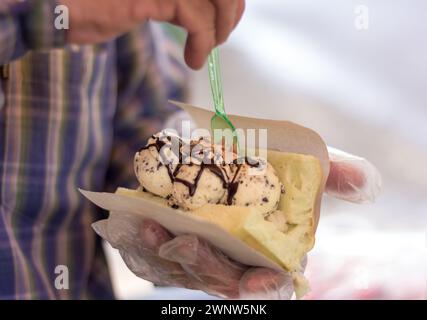 Le mani di un commerciante maschile che raccoglie il gelato con gocce di cioccolato alla vaniglia nel pane per un cliente. Foto Stock